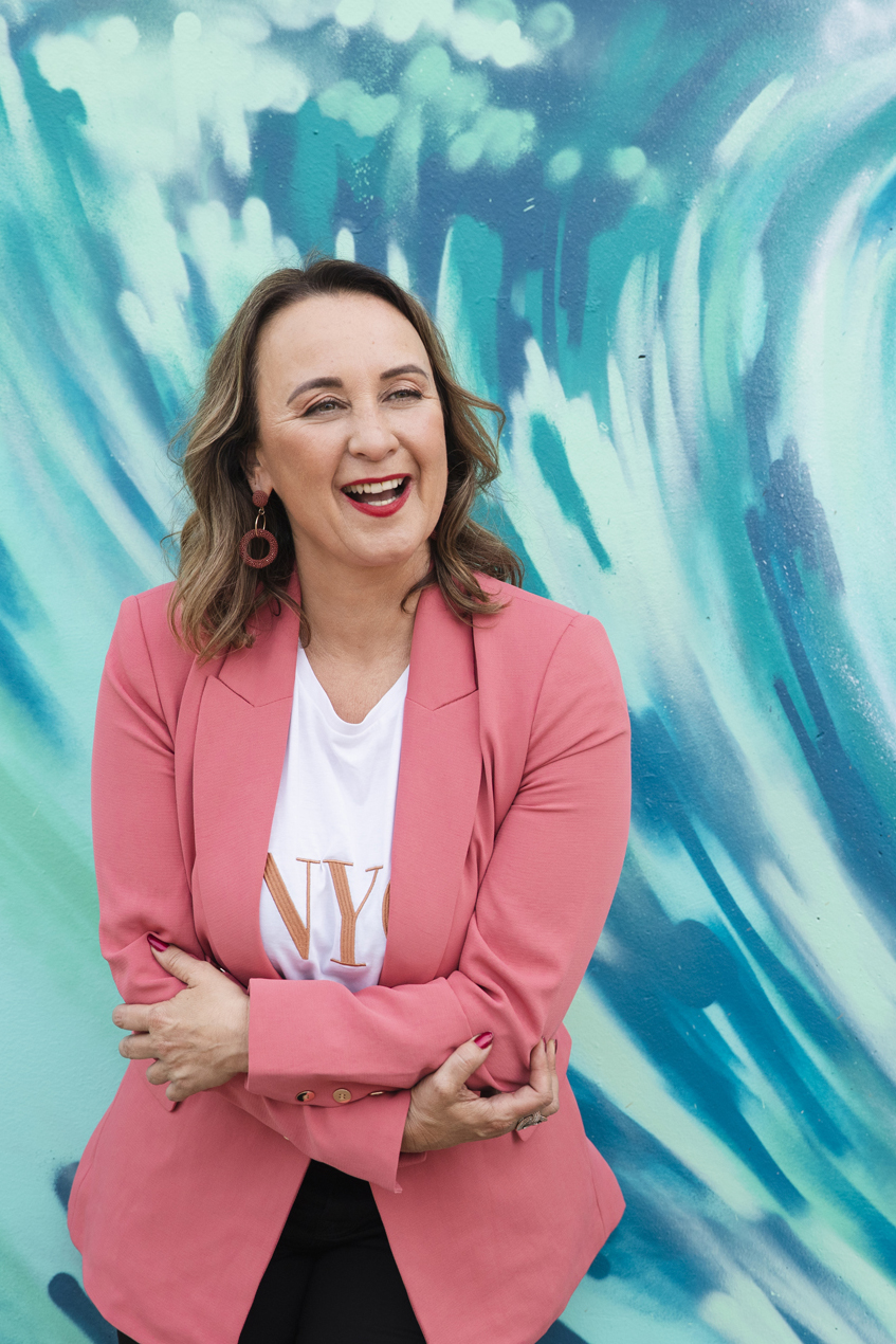 Business woman crossing arms and laughing while standing in front of a blue wall