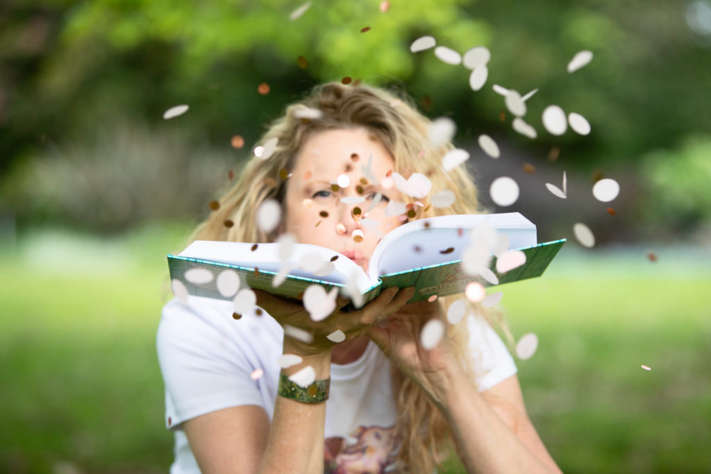 Lady holding an open book blowing confetti