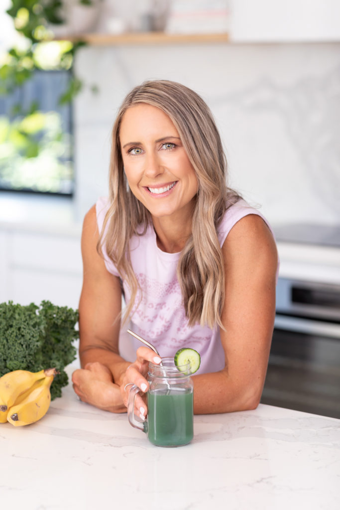 Female Nutritionist leaning at a kitchen bench and holding a green juice