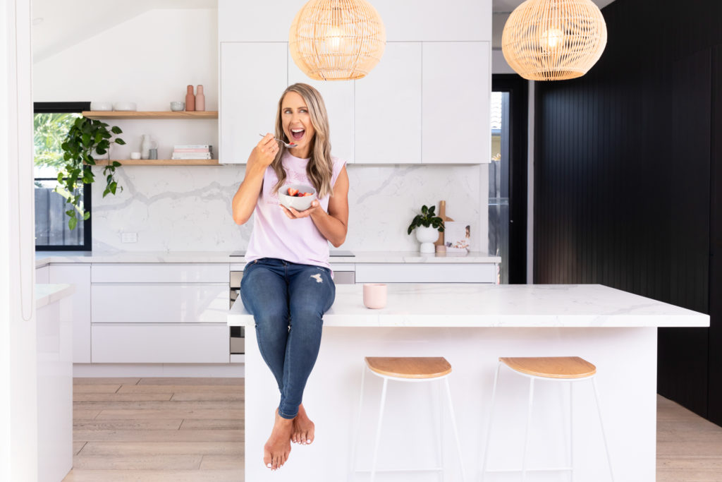 Female Nutritionist sitting on the kitchen bench with a bowl of cereal and berries