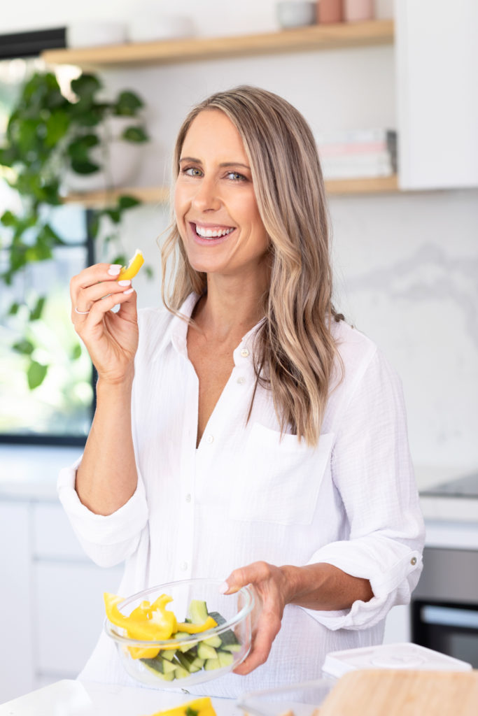 Female nutritionist holding a container of chopped capsicums and about to eat a piece