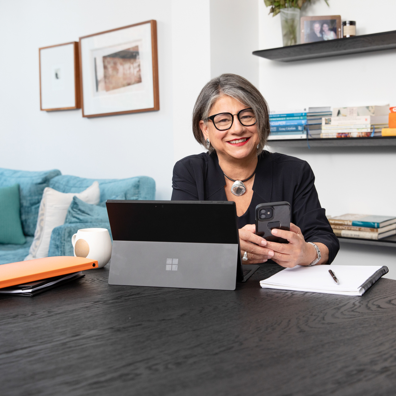 personal branding photo of a female business owner sitting at table with laptop and holding her mobile phone
