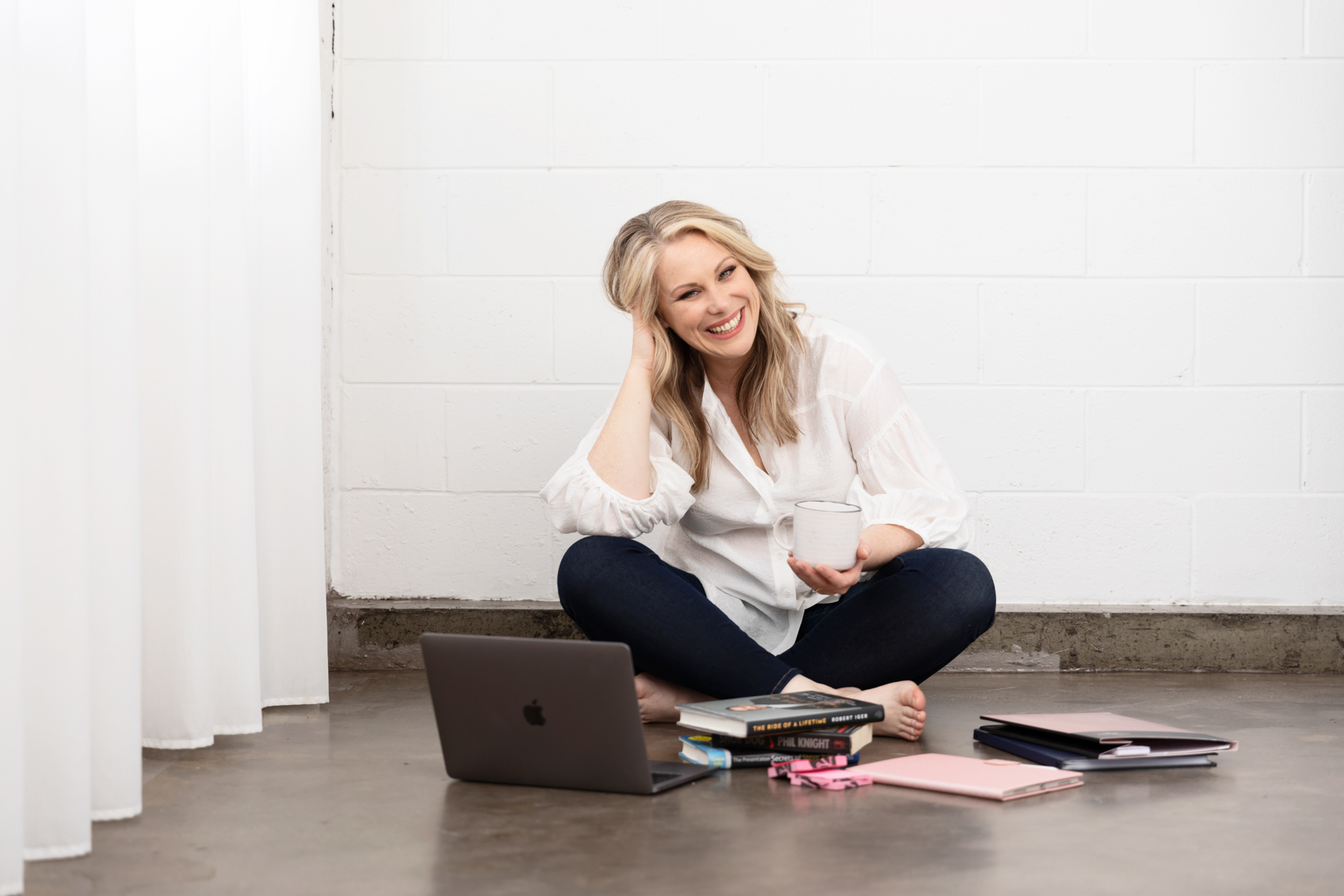 personal branding photo of a presentation coach sitting on the floor holding a cup and doing work on a laptop