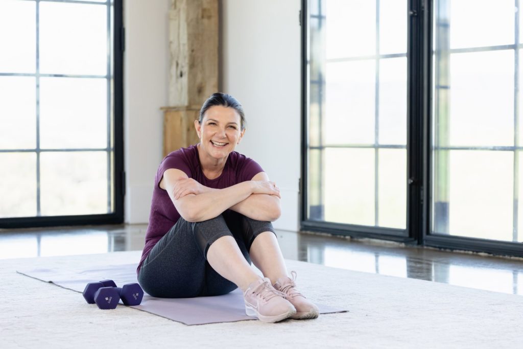 Lady sitting on yoga mat with hand weights beside her