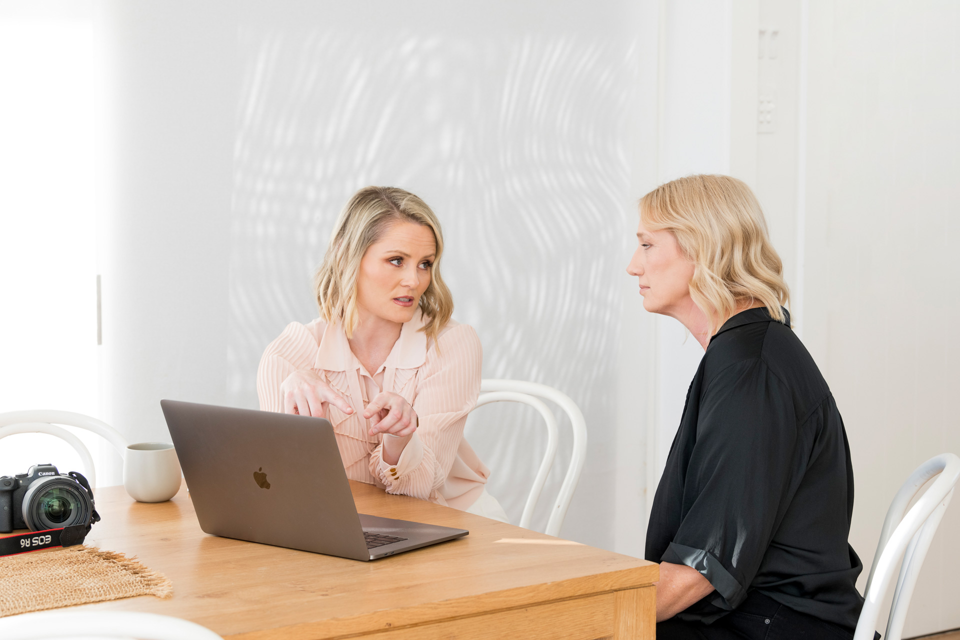 Two business women sitting at a table talking with a laptop in front of them