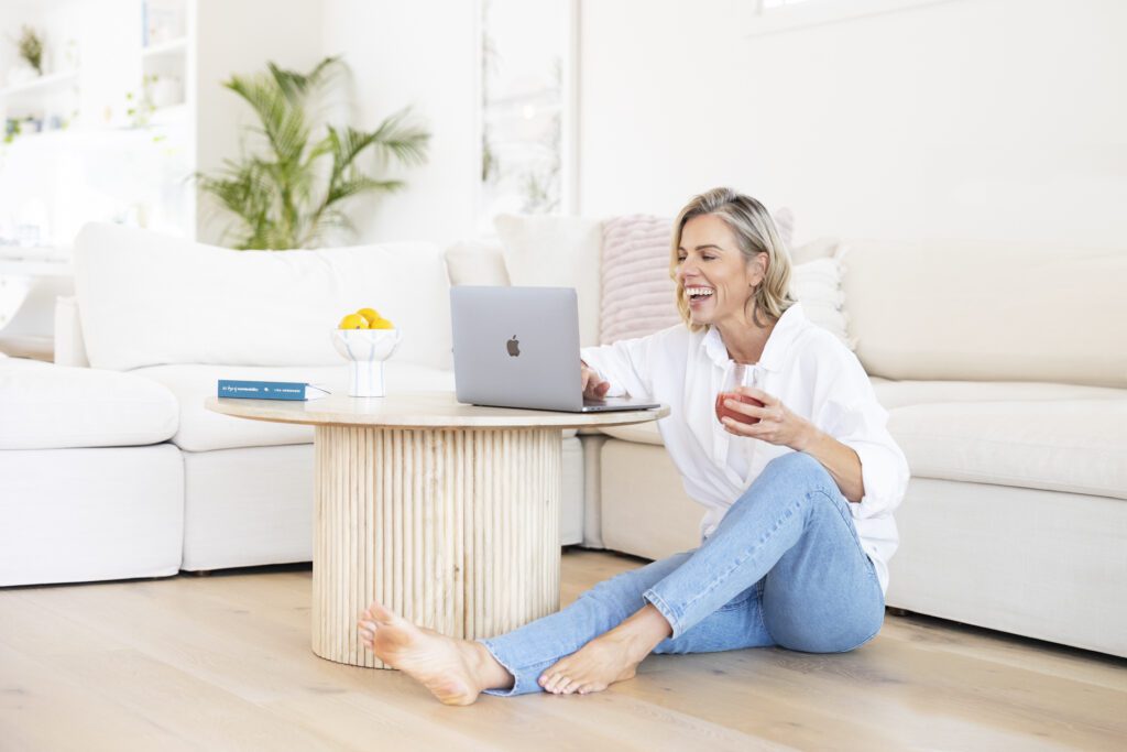 Lady sitting on the floor next to a coffee table and doing work on her laptop