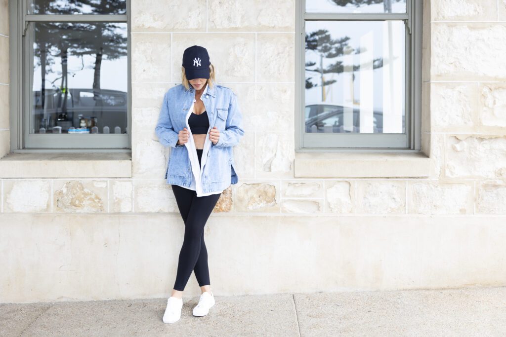 Lady leaning agains a wall wear a baseball cap