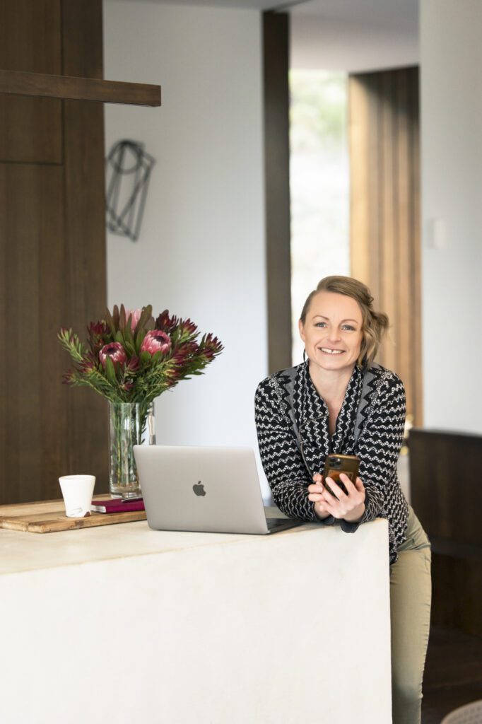 Image of a lady leaning at a kitchen bench with a mobile phone in her hand