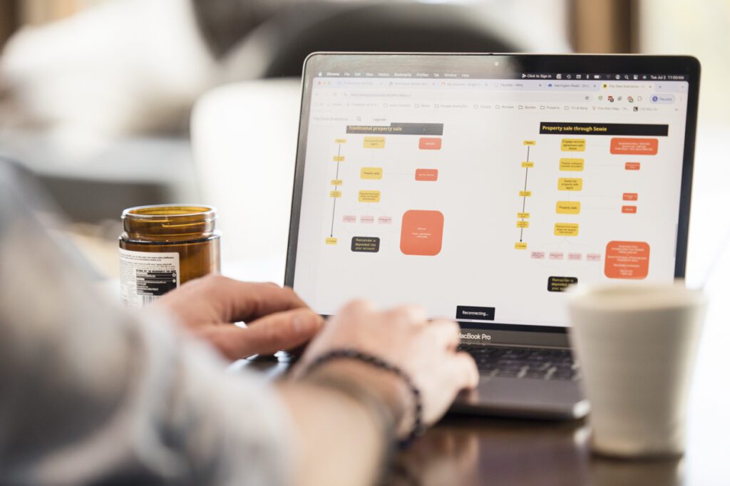 A detail shot of someone working at their laptop, their fingers are on the keyboard and there is a flowchart on the laptop screen