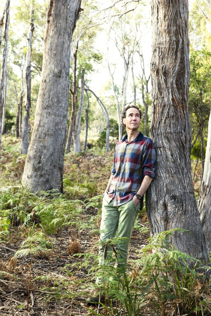 A man in a forest leaning against the trunk of a tree