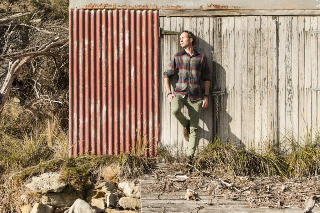 A man leaning against and old weathered boat shed