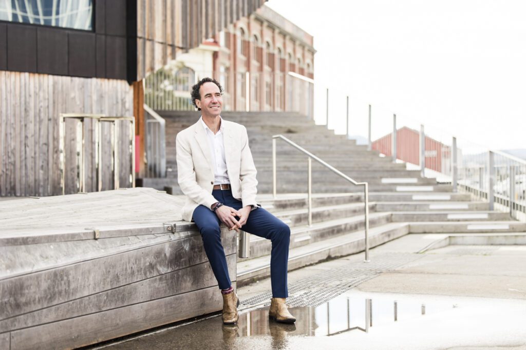 A man sitting on bench outside with buildings in the background