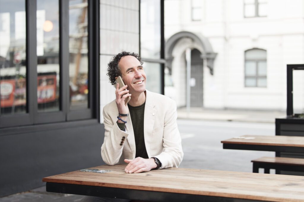 A man sitting at a table outside and talking on his mobile phone