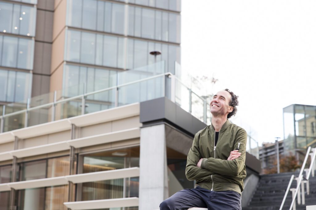 A man sitting outside looking up with buildings in the background