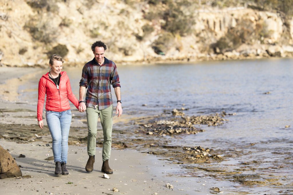 A man and a lady holding hands and walking along a beach