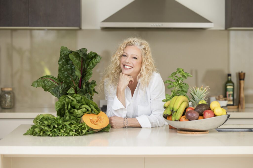 Lady wearing a white shirt standing behind a kitchen bench with fruit and vegetables - personal brand photoshoot
