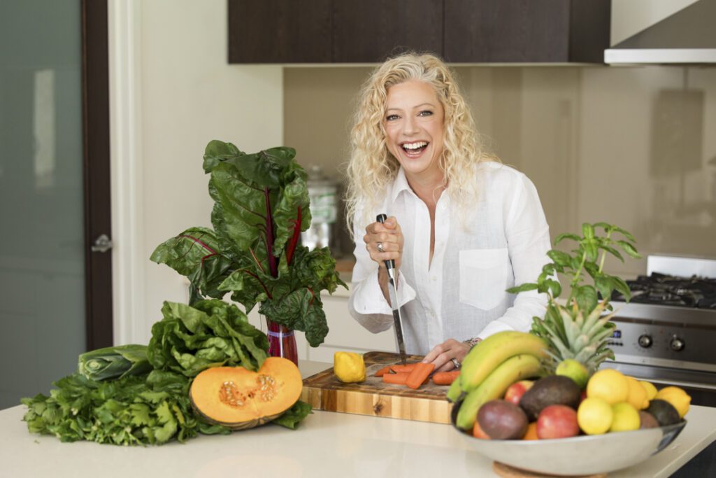 Lady wearing a white shirt standing behind a kitchen bench with fruit and vegetables chopping them up on a chopping board - personal brand photoshoot