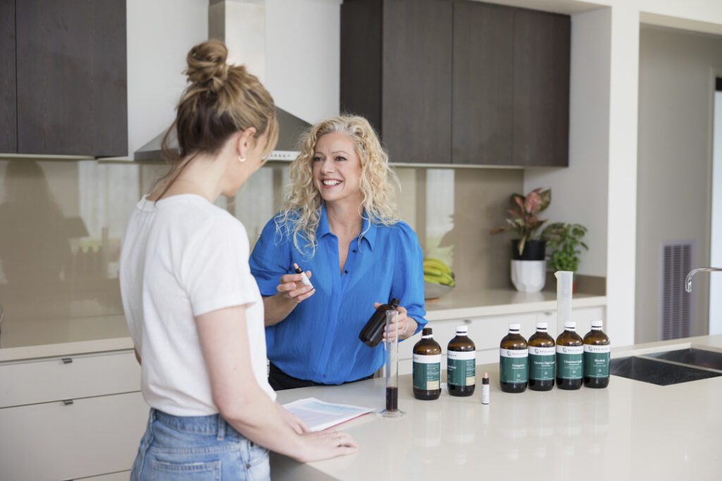 A lady wearing a blue shirt handing a bottle of oil to another lady wearing a white t-shirt - captured on a personal brand photoshoot