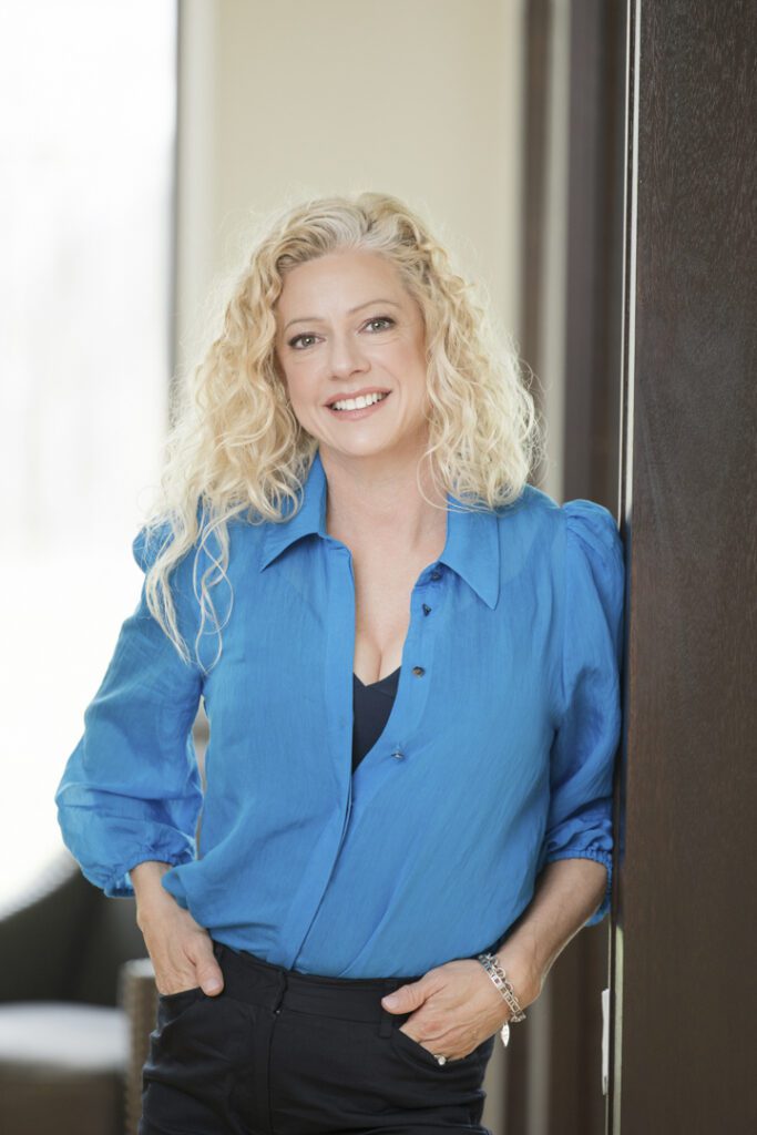 A lady wearing a blue shirt and black pants leaning against a wall - captured on a personal brand photoshoot