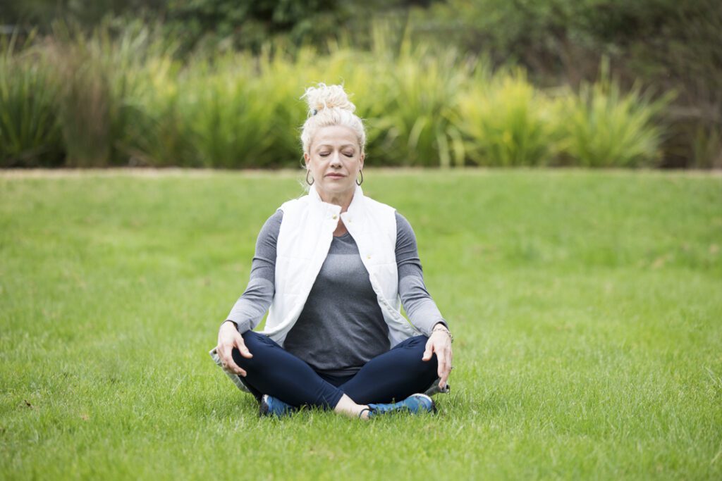 A lady wearing fitness attire sitting cross legged on the grass with eyes close and breathing deeply in meditation - personal brand photoshoot
