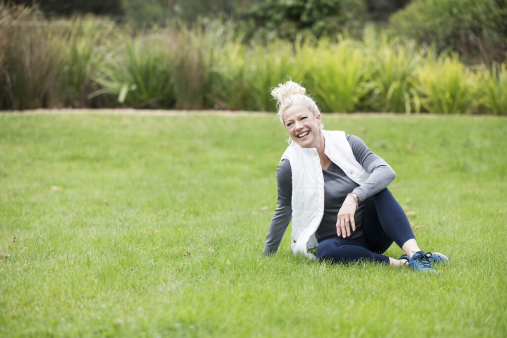 A lady wearing fitness attire, sitting on the grass and laughing - captured on a personal brand photoshoot