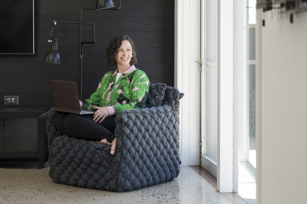 Lady in comfy chair with laptop on her knees looking out the window