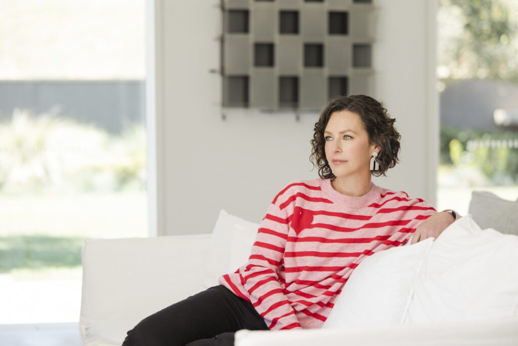 Lady wearing a pink and red stripe jumper and black jeans sitting on a white couch