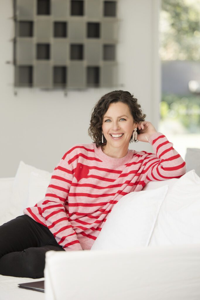 Lady wearing a pink and red stripe jumper and black jeans sitting on a white couch