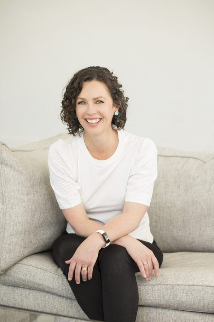 A lady wearing a white top and black jeans sitting on a couch