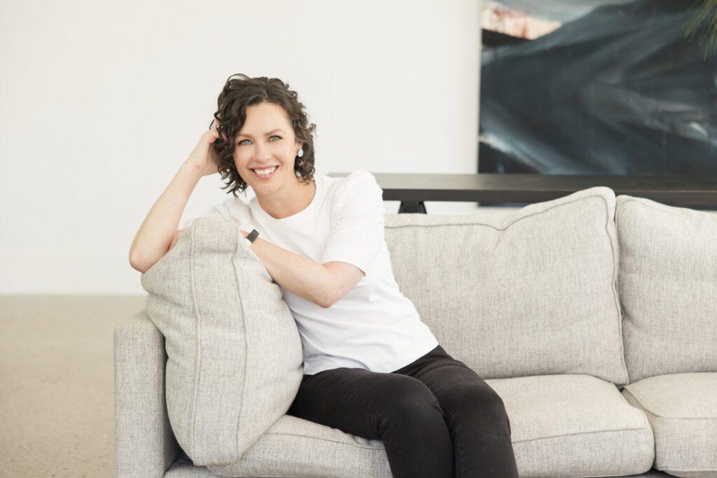 A lady wearing a white top and black jeans sitting on a couch