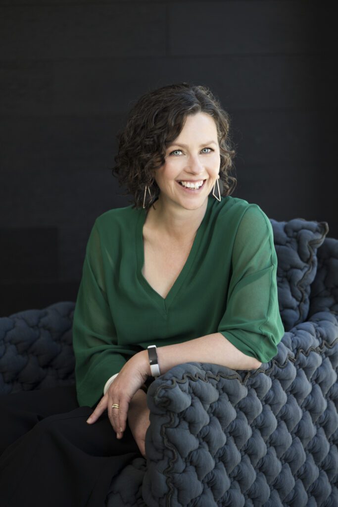 A lady wearing a green top who is sitting in a navy coloured comfy chair