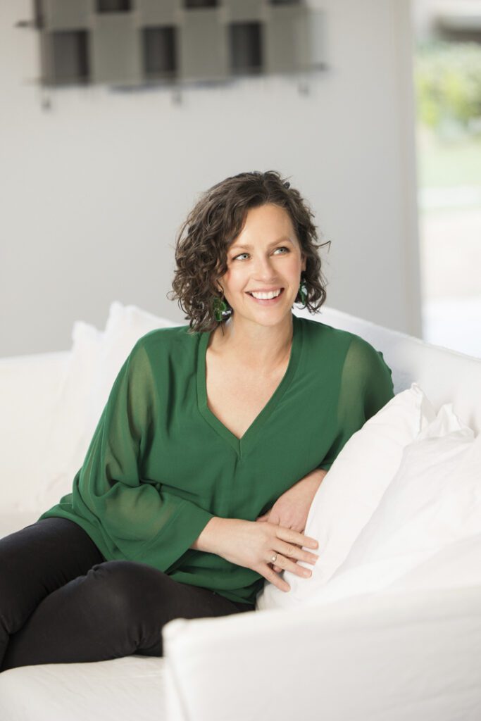 A lady wearing a green top who is sitting on a white couch