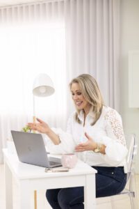 A lady wearing a white shirt and jeans sitting at her desk talking to a computer screen