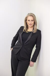 A personal brand photoshoot that captures a portrait of a lady leaning against a wall wearing a  black suit