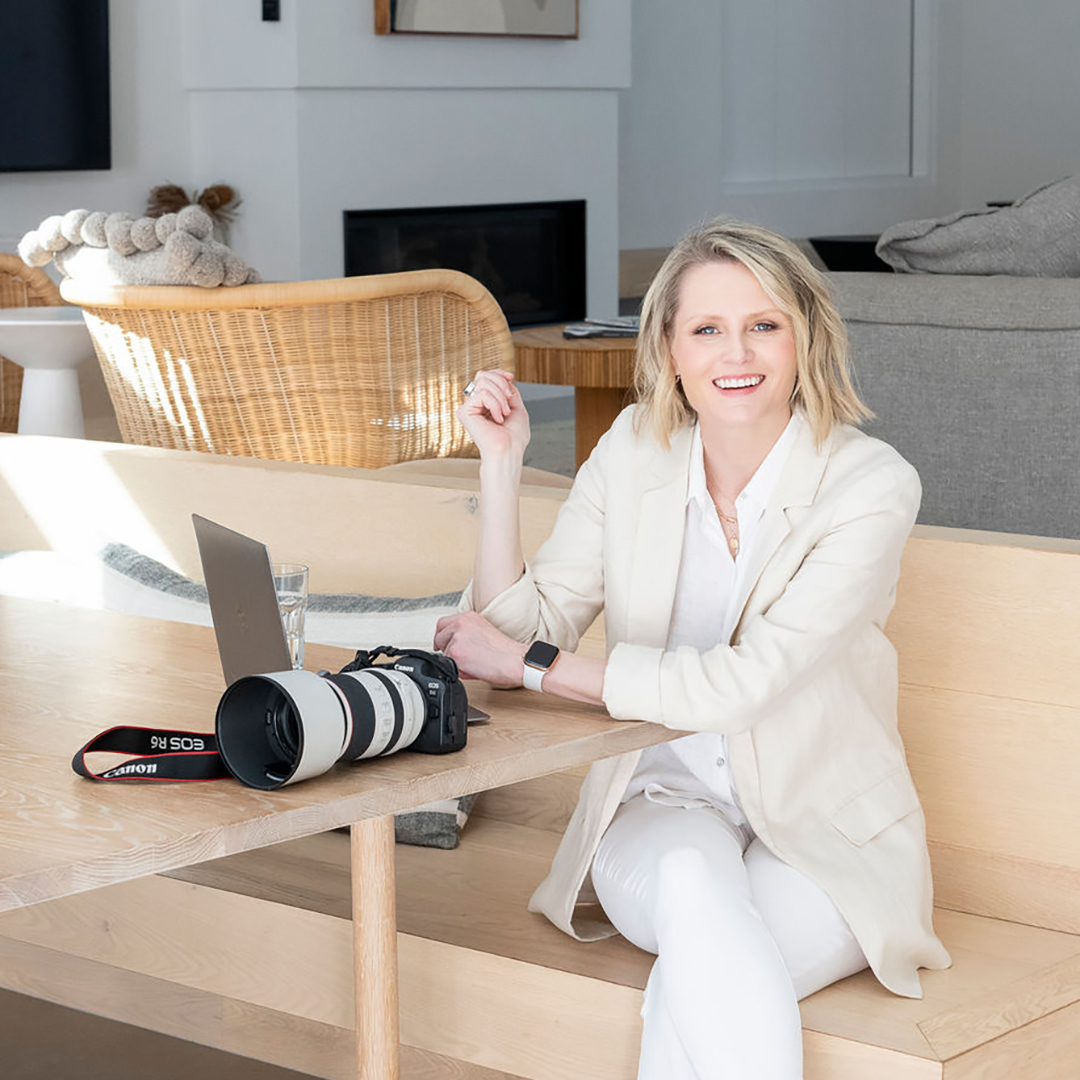 A lady sitting down at a dining table with her laptop and a camera sitting n the table