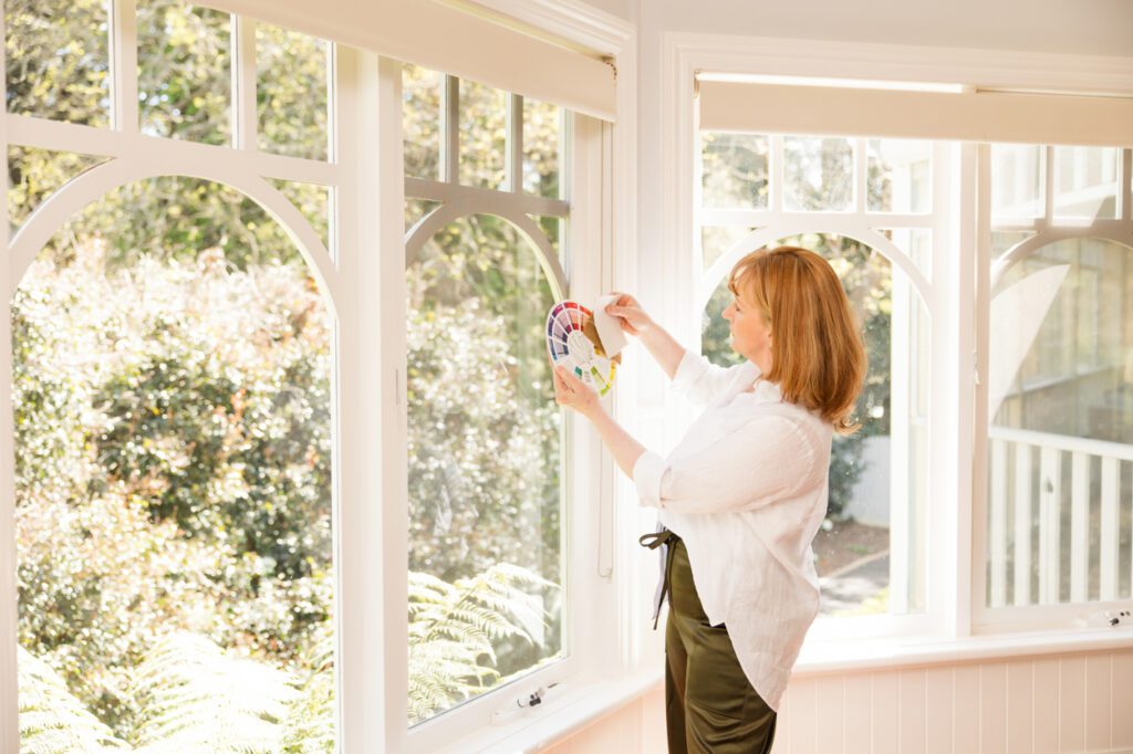 An Interior designer standing in front of windows in a heritage house looking at a colour wheel she is holding