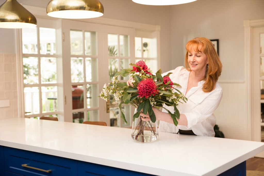 A lady with auburn coloured hair arranging a vase of flowers