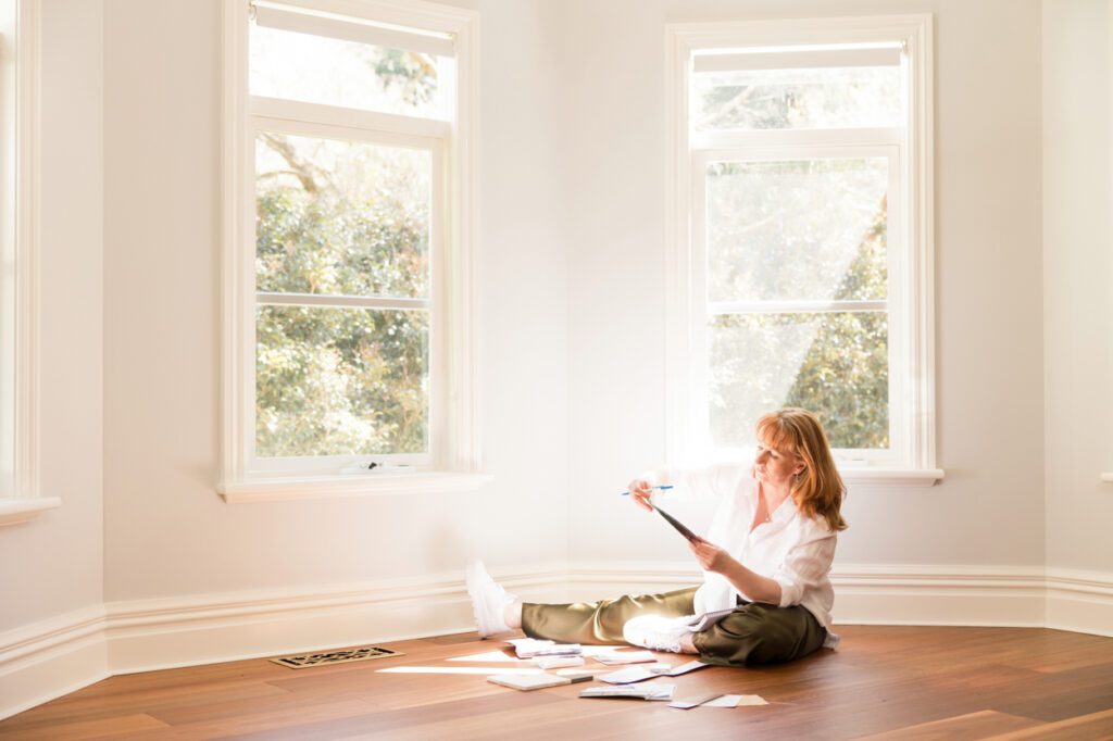 A lady sitting on a wooden floor looking a interior design samples