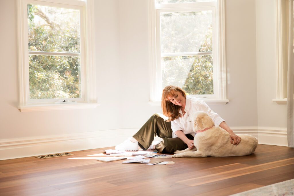 A lady sitting on a wooden floor looking a interior design samples with her golden retriever sitting beside her