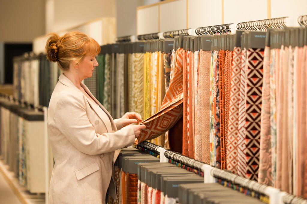 Personal Branding Photo of a female Interior designer standing looking at a rack of furnishing fabric swatches