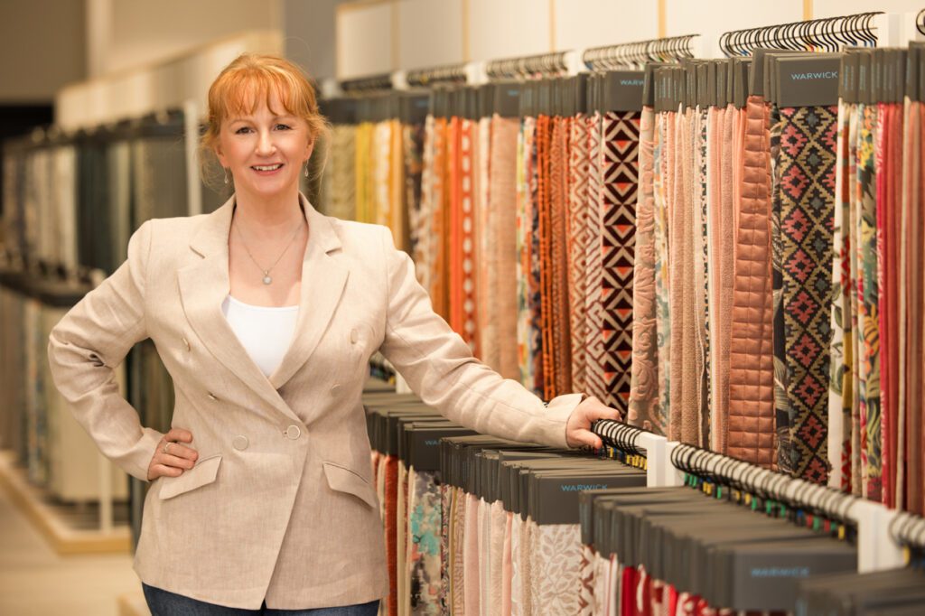 Personal Branding Photo of a female Interior designer standing in front of a stand with furnishing fabric swatches