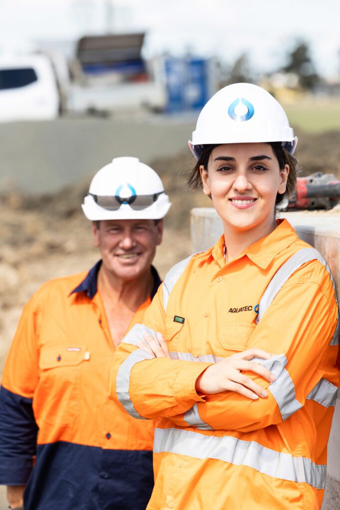 A female and a male wearing high vis clothing and hard hats