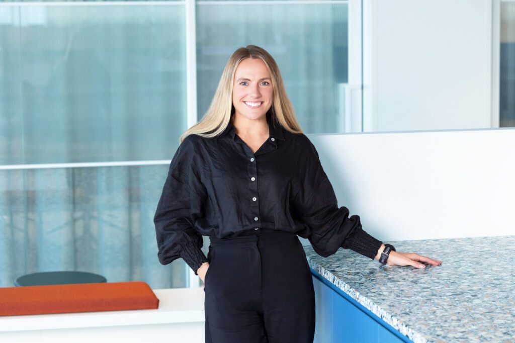 Portrait of a lady with long blonde hair wearing a black shirt and black pants