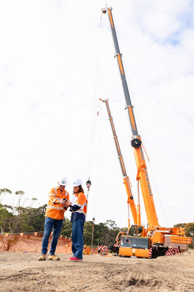 A man and a lady wearing high vis clothing and hard hats standing in front of a worksite