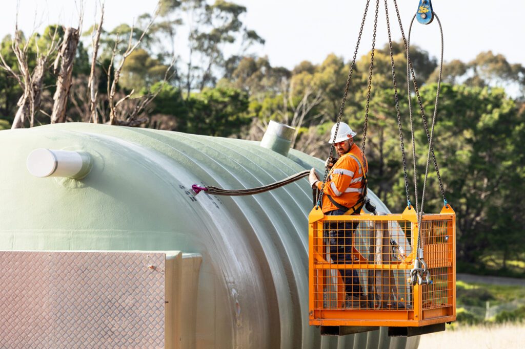 A man wearing high vis clothing and a hard hat standing in the cage of a crane