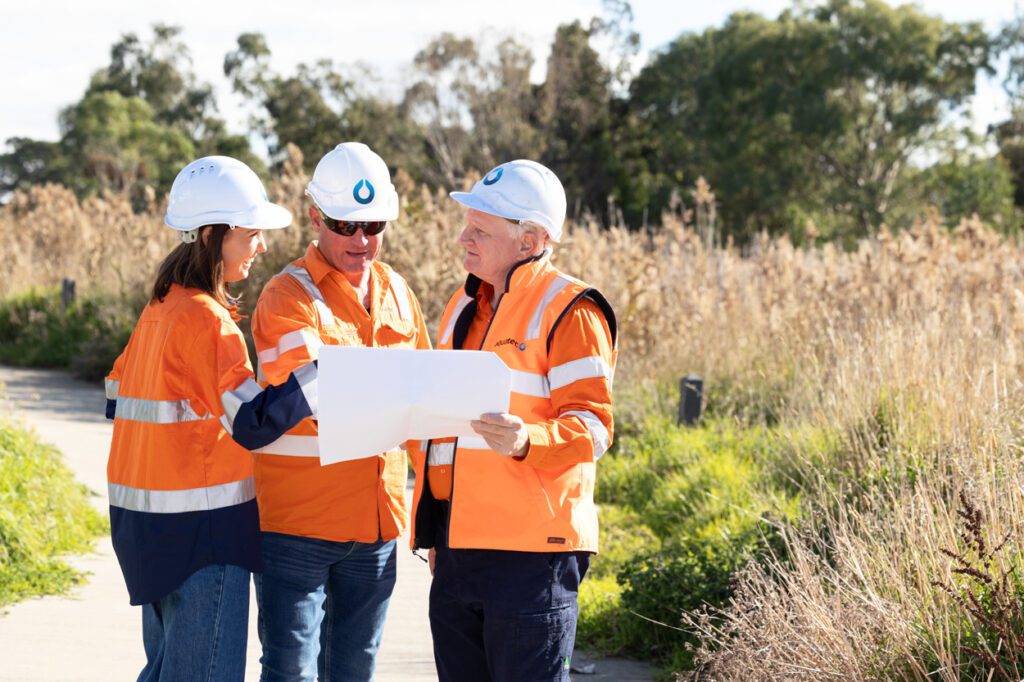 Two males and a female wearing high vis clothing and hard hats looking over work plans