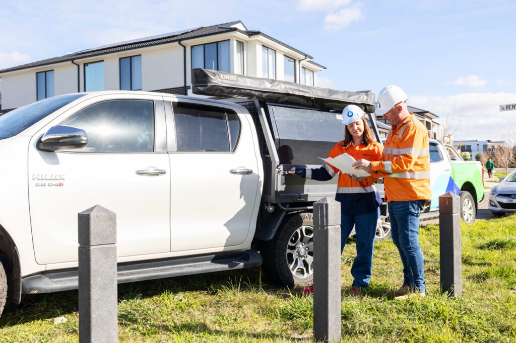 A male and a female wearing high vis clothing and looking over work plans