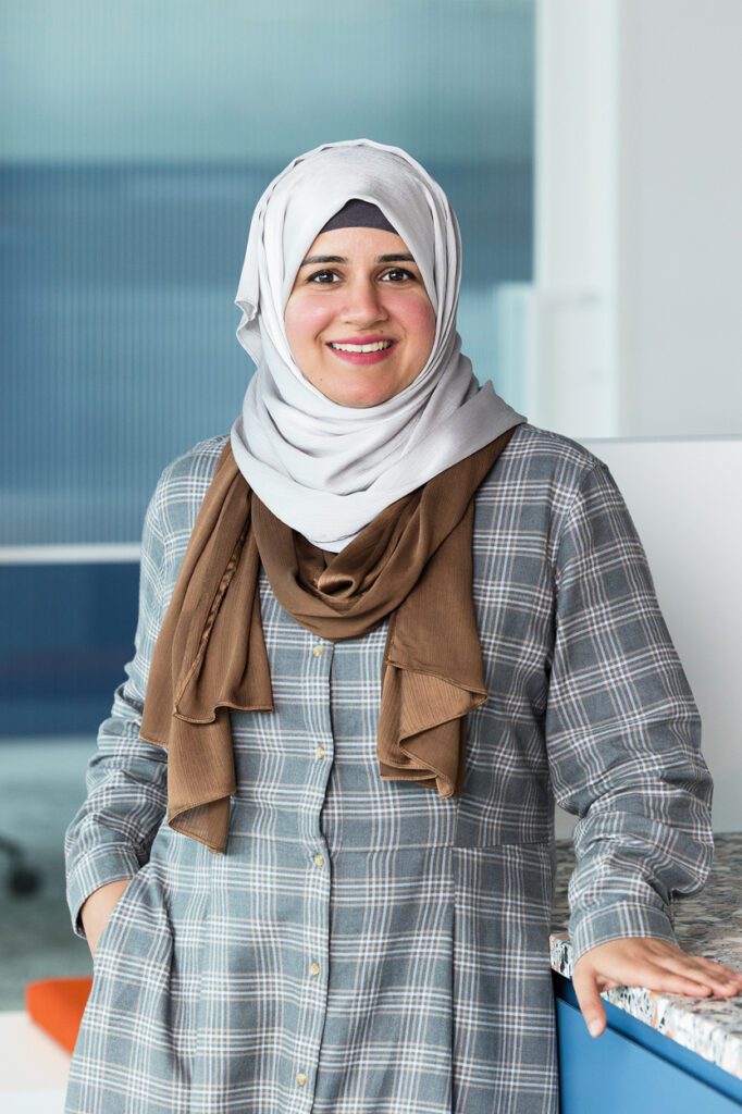 A portrait of a lady wearing a grey and white checked dress and brown and white scarves