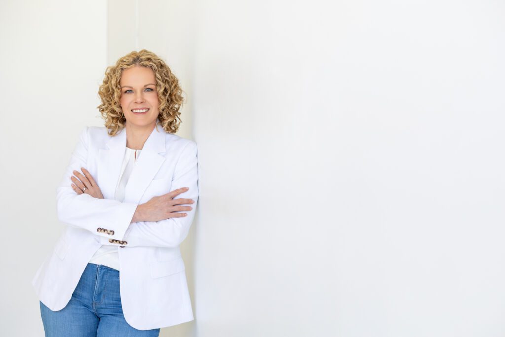 Portrait of a female entrepreneur leaning again a wall with arms crossed in front and wearing a white blazer 