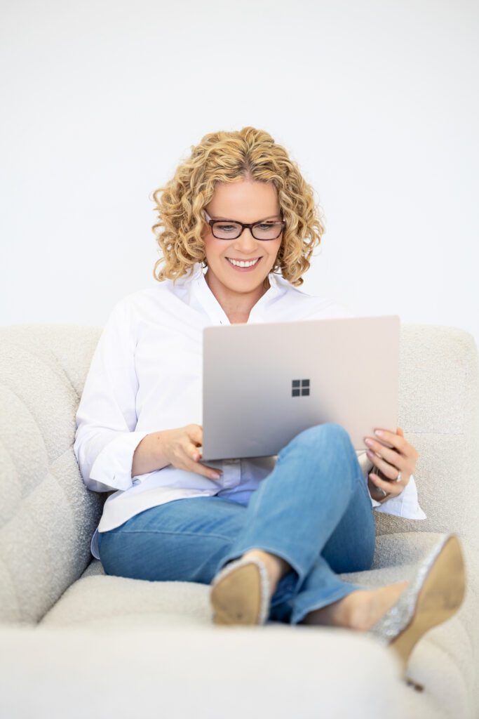 Photo of a female entrepreneur sitting on a couch with her open laptop on her legs while she is looking at the screen